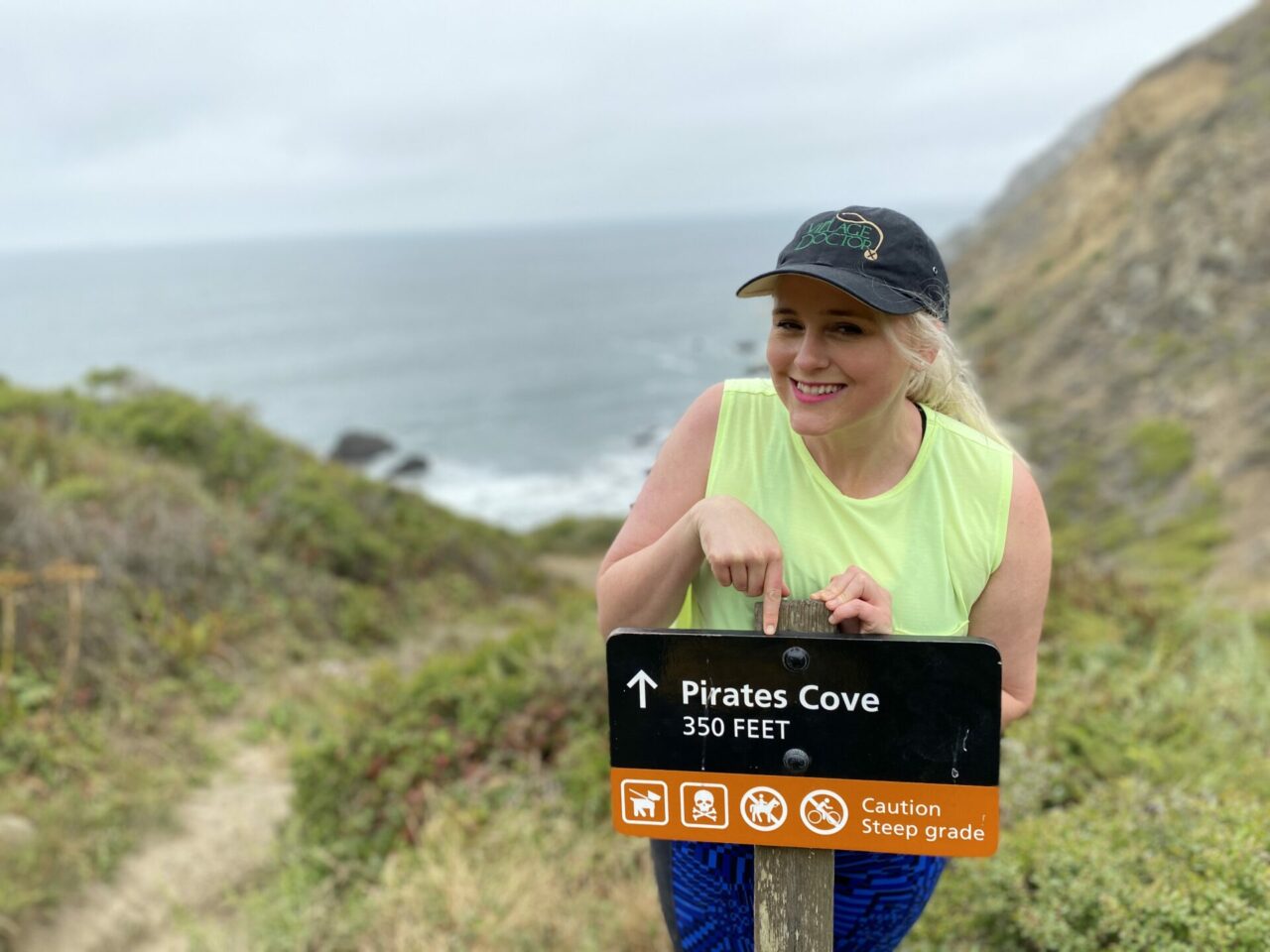 Woman in cap pointing at Pirate's Cove sign with the walkway to the beach behind