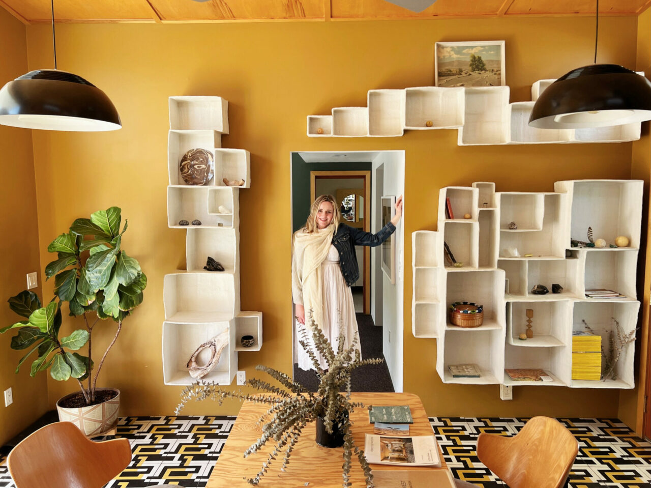 Dany leaning in doorway in Andrea Zittel home in Joshua Tree - yellow with boxes as storage and plant.